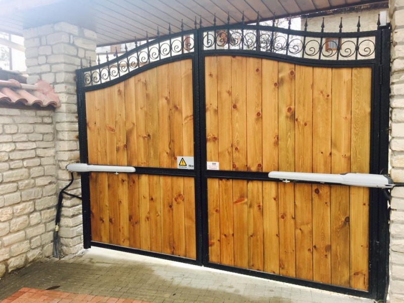 Ferforje çerçeveli ahşap çift kanatlı otomatik kapı – bahçe veya villa girişine uygun kollu motor sistemli kapı modeli